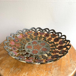 Może przedstawiać: Miska mosiężna z misternym wzorem kwiatowym w odcieniach r&oacute;żowego, zielonego i złotego. Miska ma falisty brzeg i wypukłe centrum.