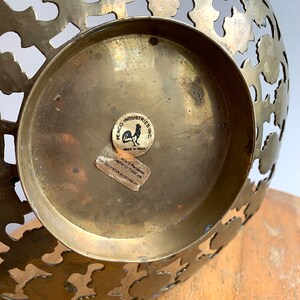 Może przedstawiać: Miska mosiężna z ozdobnym wzorem wyciętym. Miska ma naklejkę na spodzie z napisem "Penco Industries Inc. Wyprodukowano w Indiach. Artykuł jest przeznaczony do użytku z żywnością do cel&oacute;w dekoracyjnych."