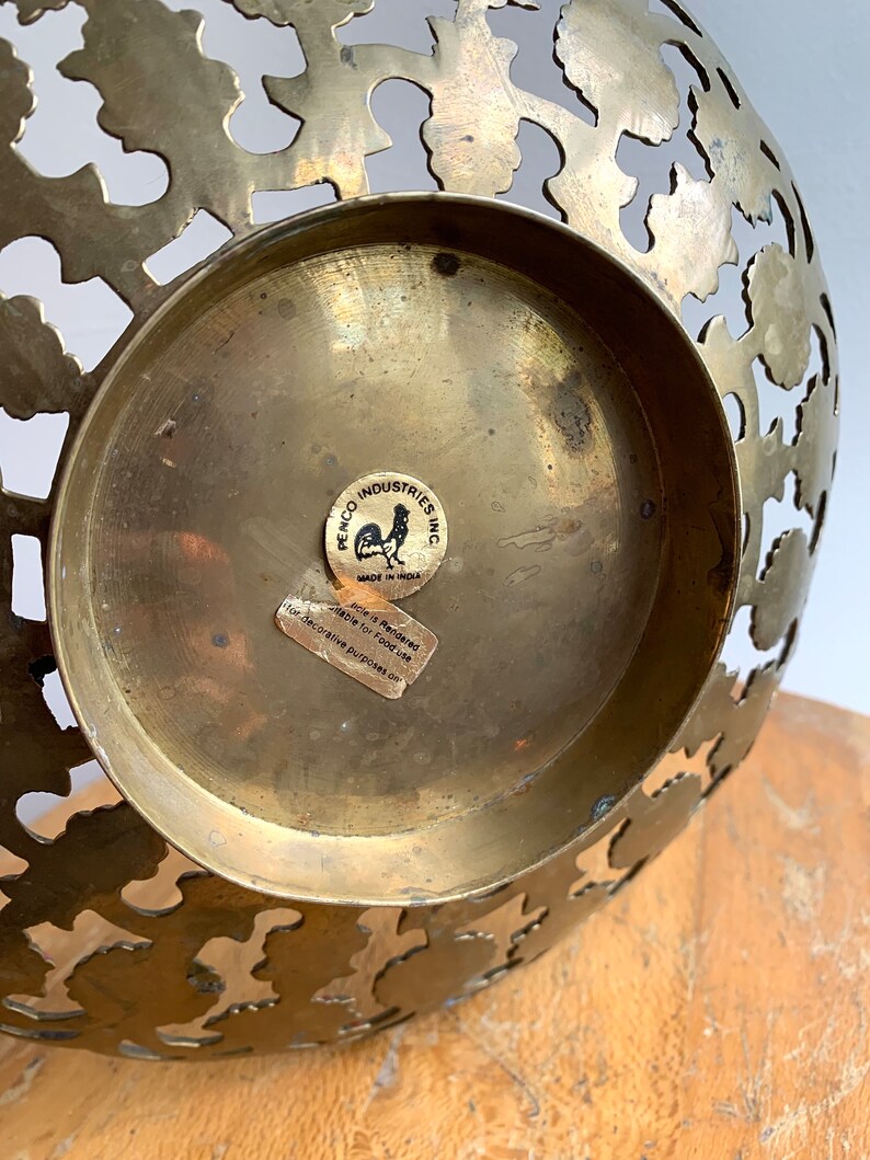 Może przedstawiać: Miska mosiężna z ozdobnym wzorem wyciętym. Miska ma naklejkę na spodzie z napisem "Penco Industries Inc. Wyprodukowano w Indiach. Artykuł jest przeznaczony do użytku z żywnością do cel&oacute;w dekoracyjnych."