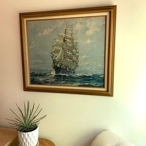 May include: A framed painting of a tall ship sailing on a blue ocean with white clouds in the sky. The ship has white sails and a brown hull. The frame is gold.