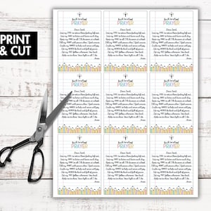 May include: A sheet of printable prayer cards with the text "Back to School Prayer" and a pencil border. The words "Print & Cut" are in a black box. Scissors are next to the sheet on a white wooden surface.