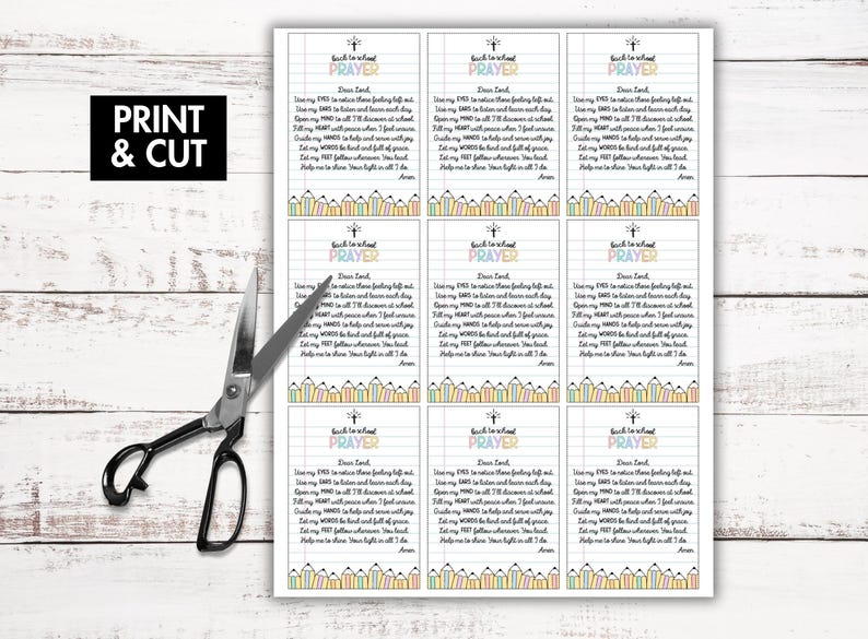 May include: A sheet of printable prayer cards with the text "Back to School Prayer" and a pencil border. The words "Print & Cut" are in a black box. Scissors are next to the sheet on a white wooden surface.