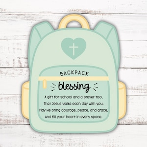 May include: A light green backpack-shaped card with a yellow handle and accents. The card features a heart with a cross and the words "BACKPACK blessing". Text below reads "A gift for school and a prayer too..." on a white wooden background.