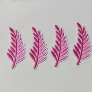 May include: Four embroidered patches featuring a pink leaf design with a white border. The leaves have a detailed, textured appearance, with a gradient of pink shades. The patches are arranged in a row against a white background.