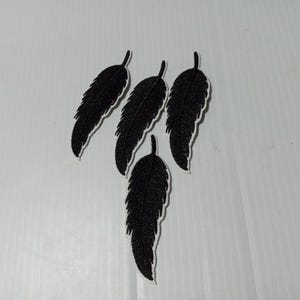 May include: Five black embroidered feather patches. The feathers are detailed with stitching and have a white outline.
