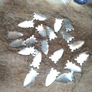 May include: A collection of silver-colored arrowheads with serrated edges, arranged on a brown fur surface.