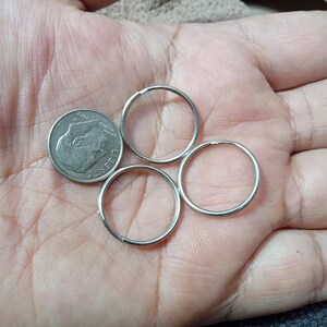 May include: Three circular silver-toned metal split rings arranged in a cluster next to a United States dime coin. The rings are thin, smooth, and feature a single coil design, providing a clear visual comparison of their size relative to the coin.