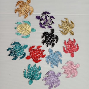 May include: A collection of embroidered turtle patches in various colors, including gold, purple, black, red, blue, and pink. Each patch features detailed stitching and a textured appearance, suitable for embellishing clothing or accessories.