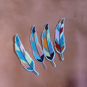 May include: Four colorful feather patches with intricate embroidery in shades of blue, yellow, orange, pink, and red. Each patch has a white border and is set against a brown leather-like surface.