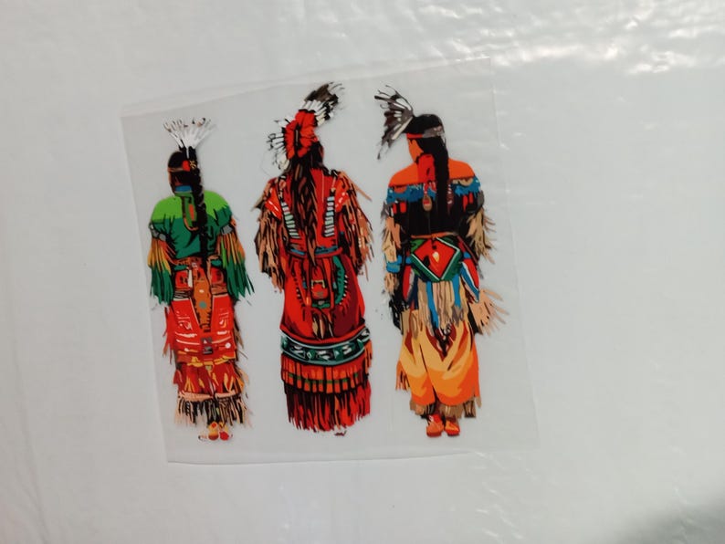 May include: A colorful illustration of three figures in traditional Native American attire. The figures are seen from the back, showcasing detailed clothing in shades of red, green, orange, and blue, with feathered headdresses.