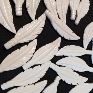 May include: A collection of white carved bone feathers. The feathers are detailed with lines and have a smooth, polished finish.