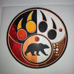 May include: A round wooden art piece featuring a bear paw print design with a bear silhouette in the center. The design incorporates various colors and textures, including black, white, red, and brown, with a circular border.