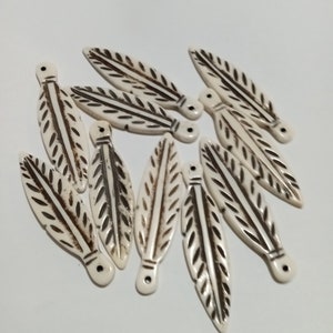 May include: A group of white bone leaf-shaped beads with brown etched details. The beads have a hole at the top for stringing.