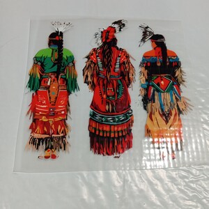 May include: Three colorful Native American figures in traditional attire. The figures are depicted from the back, showcasing detailed clothing with feathers, fringe, and intricate patterns. The color palette includes green, red, orange, and blue, creating a vibrant and cultural image.