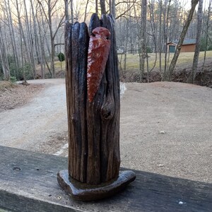 May include: A dark brown wooden sculpture with a red arrowhead embedded in it. The sculpture is sitting on a wooden surface.