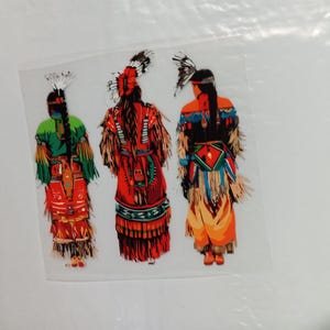 May include: A colorful illustration of three figures in traditional Native American attire. The figures are seen from the back, showcasing detailed clothing in shades of red, green, orange, and blue, with feathered headdresses.