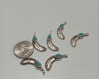 May include: Silver-toned feather pendants with turquoise-colored accents. The pendants are arranged on a white surface next to a U.S. quarter coin. The feathers have detailed veining.