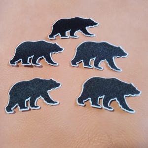 May include: Five black bear silhouette iron-on patches on a light orange background.