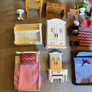 May include: A collection of miniature dollhouse furniture including a white wardrobe, a white vanity with a stool, a bed with a pink gingham quilt, a bed with a blue plaid quilt, a white piano, a brown hutch, a wooden chair, and a pink toy car.