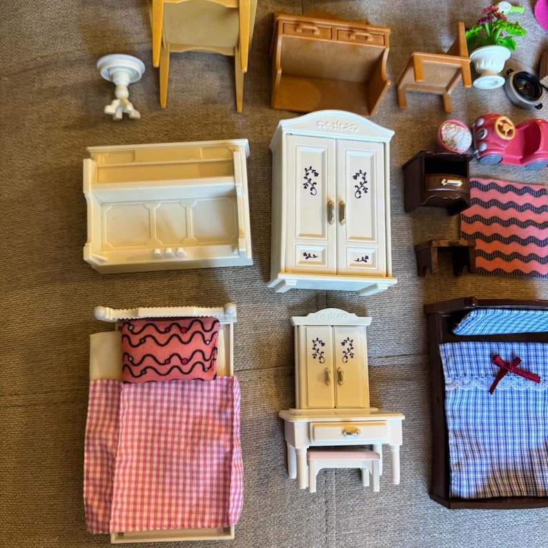 May include: A collection of miniature dollhouse furniture including a white wardrobe, a white vanity with a stool, a bed with a pink gingham quilt, a bed with a blue plaid quilt, a white piano, a brown hutch, a wooden chair, and a pink toy car.