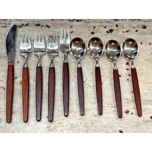 May include: A set of vintage silverware with stainless steel heads and dark wood handles. The set includes a knife, forks, and spoons. The silverware is arranged on a speckled surface.