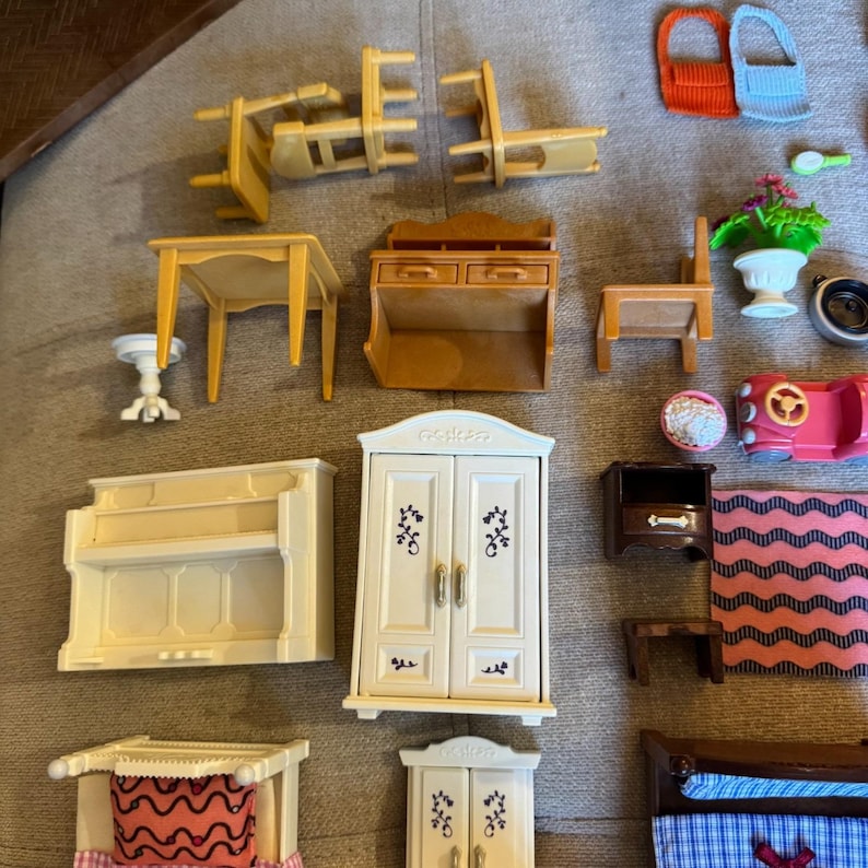 May include: A collection of miniature dollhouse furniture and accessories including a light brown table, chairs, a hutch, a white wardrobe, a piano, a bed with a blue plaid blanket, a pink car, a potted plant, and various small household items.