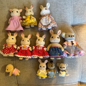 May include: A collection of twelve miniature flocked animal figurines dressed in various outfits. The group includes rabbits, koalas, and a small dog, wearing dresses with patterns like gingham, polka dots, and floral prints, along with small rompers.