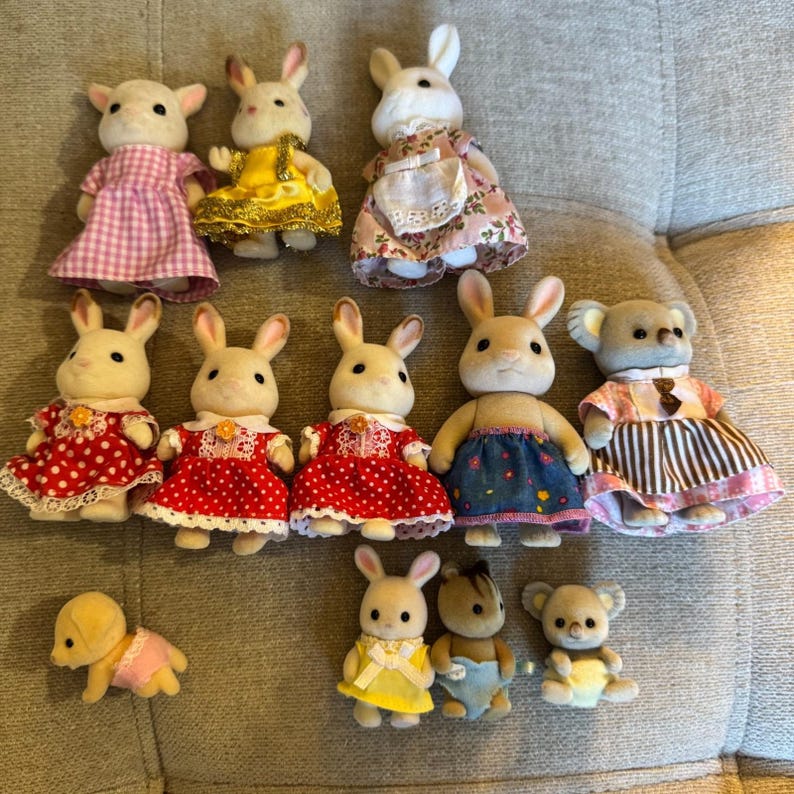 May include: A collection of twelve miniature flocked animal figurines dressed in various outfits. The group includes rabbits, koalas, and a small dog, wearing dresses with patterns like gingham, polka dots, and floral prints, along with small rompers.