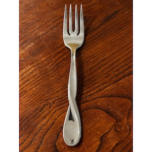 May include: A silver fork with a twisted handle, resting on a wooden surface. The fork has four tines and a polished finish. The handle has a unique, elegant design.