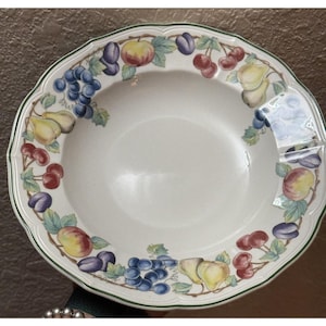 May include: White ceramic serving bowl with a scalloped edge and a green trim. The bowl is decorated with a colorful fruit design featuring grapes, cherries, plums, apples, and pears. A decorative piece for the kitchen or dining room.