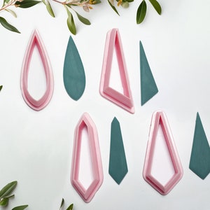 Op de afbeelding: Een set van acht roze en groene plastic koekjesuitstekers in verschillende vormen, waaronder traan-, driehoek- en ruitvormen.
