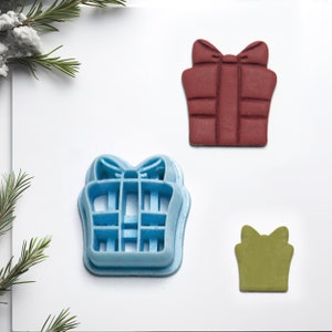 May include: Three different cookie cutters shaped like presents. The largest cutter is red, the medium cutter is blue, and the smallest cutter is green.