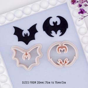 May include: Four bat-shaped items. Two are black cutouts, and two are pink cookie cutters. The text at the bottom reads "SIZES FROM 20mm/.75in TO 75mm/3in". The items are arranged on a light blue surface within a white frame.