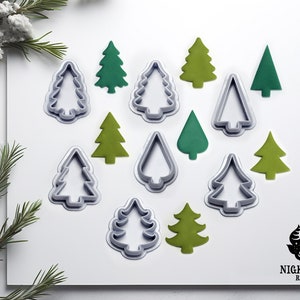 Könnte beinhalten: Ein Set mit 11 Weihnachtsbaum-Ausstechern in verschiedenen Größen und Stilen. Die Ausstecher sind aus Metall und haben eine silberne Oberfläche. Die Ausstecher sind auf einer weißen Oberfläche mit grünen Filz-Weihnachtsbäumen angeordnet.
