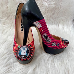 May include: Pair of Ferde platform heels with a casino theme. The heels feature a black platform and heel, with a red and pink patterned upper. The pattern includes playing cards, dice, and a roulette wheel with a rabbit.