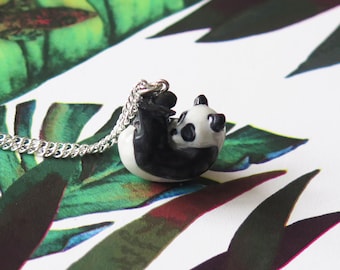 Peut inclure: Un collier en chaîne argent avec un pendentif en céramique en forme de panda. Le panda est noir et blanc et est enroulé en boule.