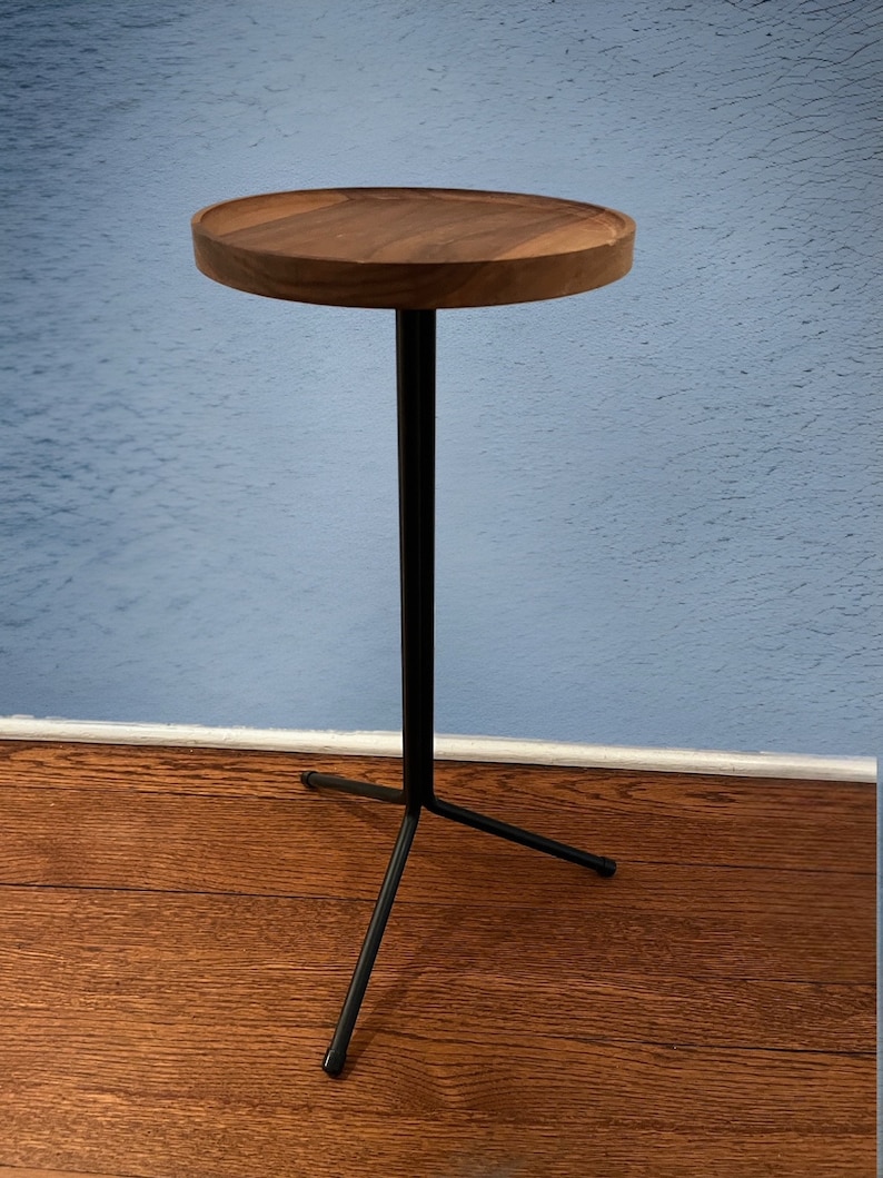 May include: A small, round side table with a dark wood top and a black metal base. The tabletop is approximately 40 cm in diameter. The base has a tripod design for stability, a stylish accent piece.