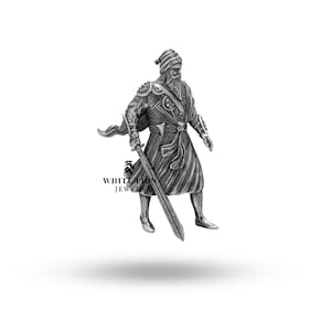 May include: A silver figurine of a warrior holding a sword. The warrior is wearing a turban and a long robe. The figurine is standing on a white background.