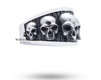 May include: A silver ring with four detailed skull designs. The skulls are arranged in a row and have a textured finish.