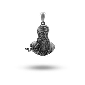 May include: Silver pendant featuring a detailed bust of a bearded man wearing a turban. The pendant is a religious symbol and is likely made for a necklace.