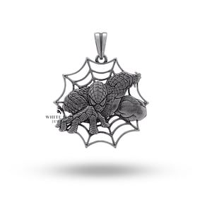 Può includere: Un ciondolo d'argento con una rappresentazione dettagliata di Spiderman in una ragnatela. Il ciondolo è progettato in stile 3D, con Spiderman che sembra strisciare fuori dalla ragnatela.