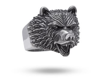 May include: A silver-toned ring featuring a detailed, three-dimensional bear head design. The bear is depicted with a snarling expression, bared teeth, and textured fur detailing across the entire surface of the ring band and head.