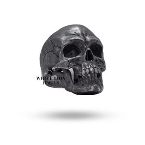 Puede incluir: Un anillo de calavera de plata detallado con una superficie texturizada. El anillo es una pieza llamativa con una estética gótica.