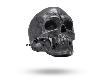 May include: A detailed silver skull ring with a textured surface. The ring is a statement piece with a gothic aesthetic.