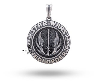 May include: A silver pendant featuring the Star Wars Jedi Order symbol. The symbol is a black and white stylized image of a lightsaber and two wings. The pendant is round and has the words "Star Wars Jedi Order" inscribed around the edge.