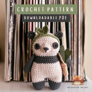 Puede incluir: Un oso panda tejido a ganchillo con una diadema de hojas verdes y una zanahoria beige. El panda es negro, blanco y gris. La imagen incluye el texto "CROCHET PATTERN DOWNLOADABLE PDF" en la parte superior y el texto "MUSHABOOM THREADS" en la parte inferior.