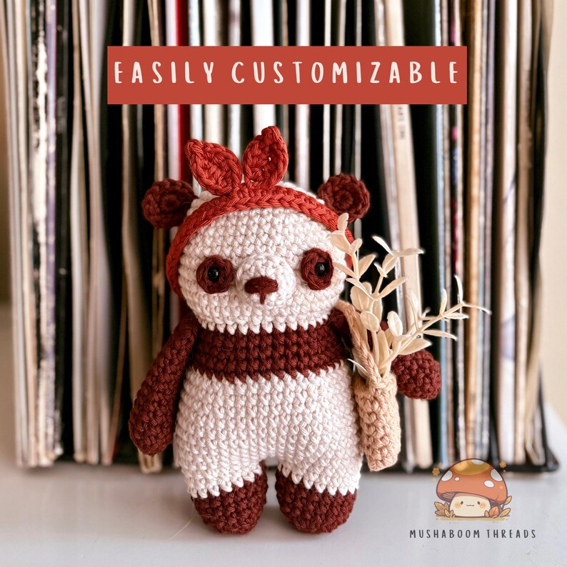 Puede incluir: Un oso panda de ganchillo hecho a mano, con una combinaci&oacute;n de colores rojo y blanco. El panda lleva un gorro rojo con orejas y sostiene un peque&ntilde;o ramo de flores secas. El texto "EASILY CUSTOMIZABLE" se muestra encima del panda.