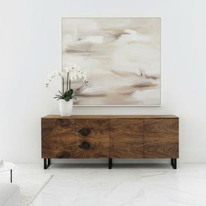 Könnte beinhalten: Ein modernes Wohnzimmer mit einem Holzschrank mit drei Türen und schwarzen Beinen. Über dem Schrank hängt ein abstraktes Gemälde. Eine weiße Orchidee steht oben auf dem Schrank. Zwei graue Sofas und ein weißer Hocker vervollständigen den Raum.