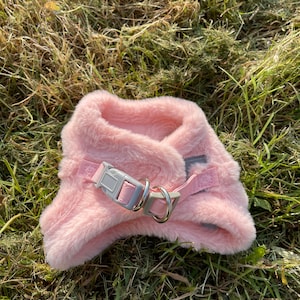 May include: A pink faux fur dog harness with a silver metal ring and a gray plastic buckle.