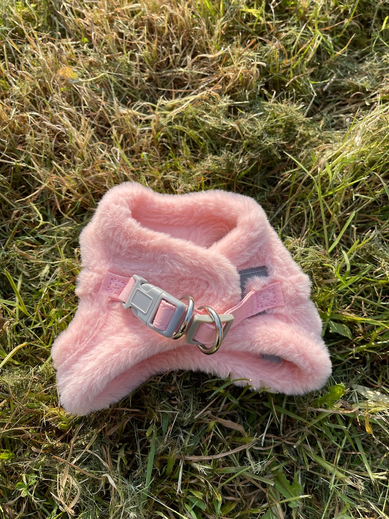May include: A pink faux fur dog harness with a silver metal ring and a gray plastic buckle.